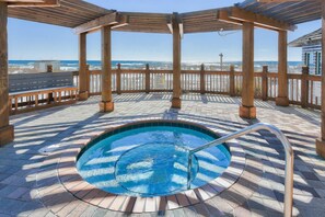 Eine Holzterrasse mit Whirlpool, einer Holzpergola und Blick auf den Strand.