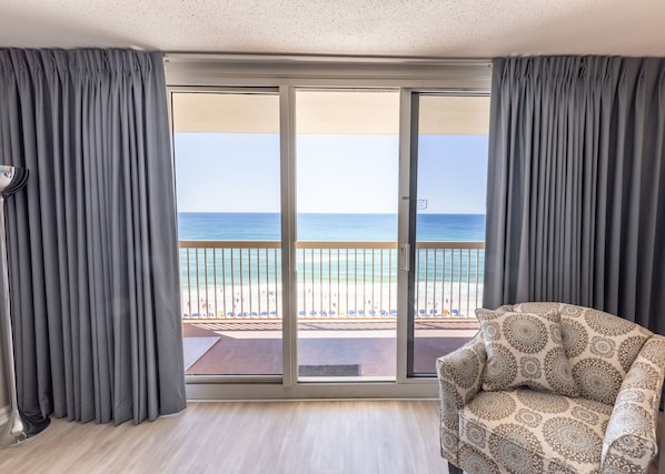A room with a large sliding glass door leading to a balcony with a view of the beach.