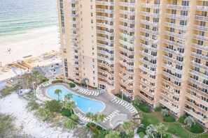 Ein Hochhaus-Hotel mit Pool, umgeben von Liegestühlen und Palmen, mit Blick auf einen Strand.