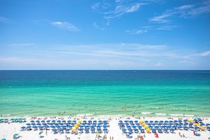 Een strand met helder turquoise water, een zandstrand en veel parasols.