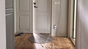 Un couloir doté d’un plancher en bois, d’une porte blanche ornée d’une fenêtre en forme de losange et d’une prise électrique sur le mur.