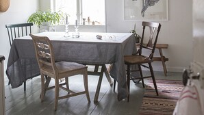Un coin repas avec une table dressée pour quatre personnes, entourée de chaises en bois, d’un luminaire suspendu et d’une estampe botanique encadrée accrochée au mur.