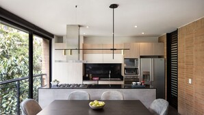 A modern kitchen with a dining area, featuring a large island, built-in appliances, and a view of greenery outside. -  ATTIK SUPERIOR -501 (Bogotá)