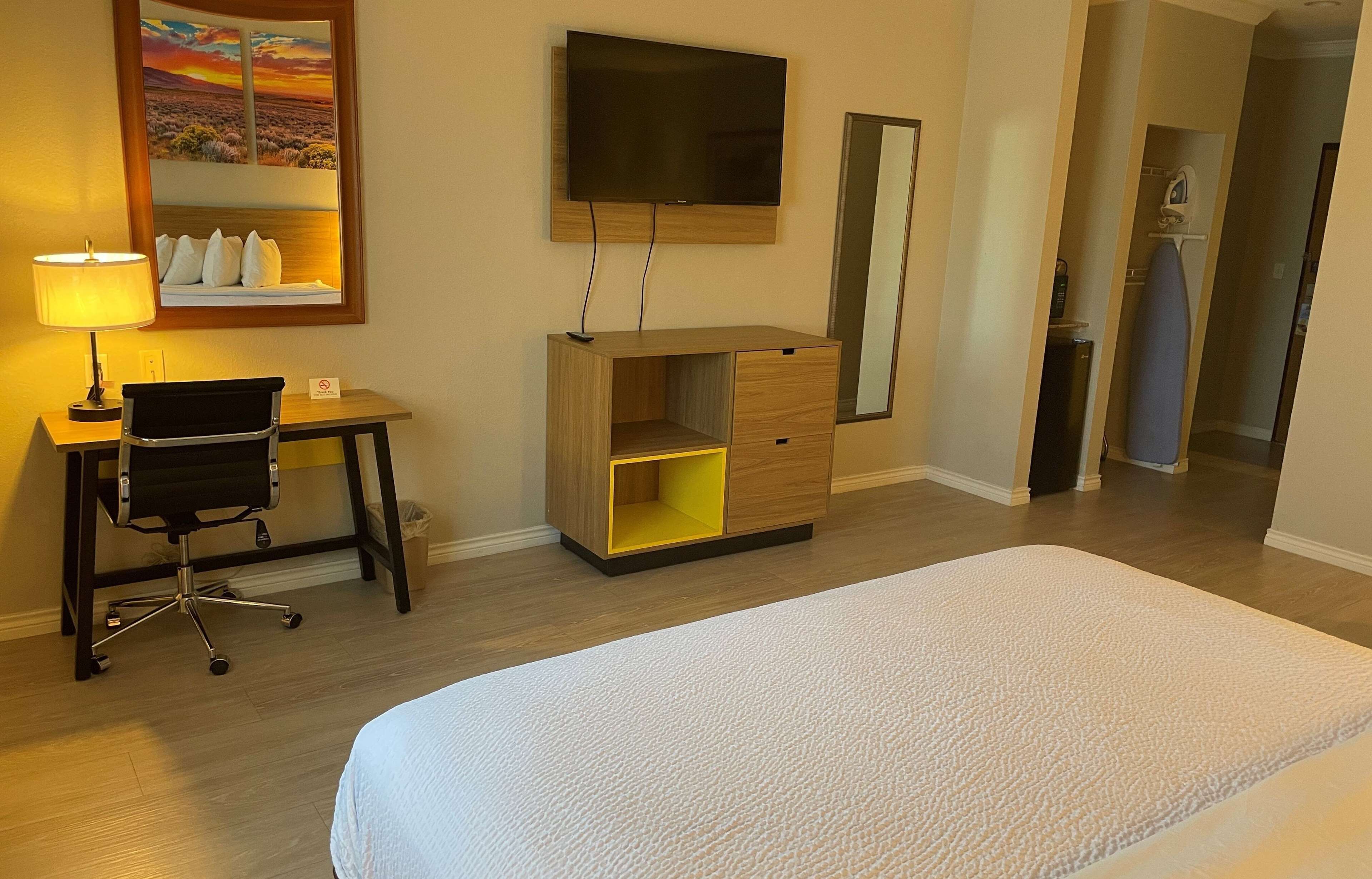 A hotel room with a bed, desk, chair, TV, and a mirror.