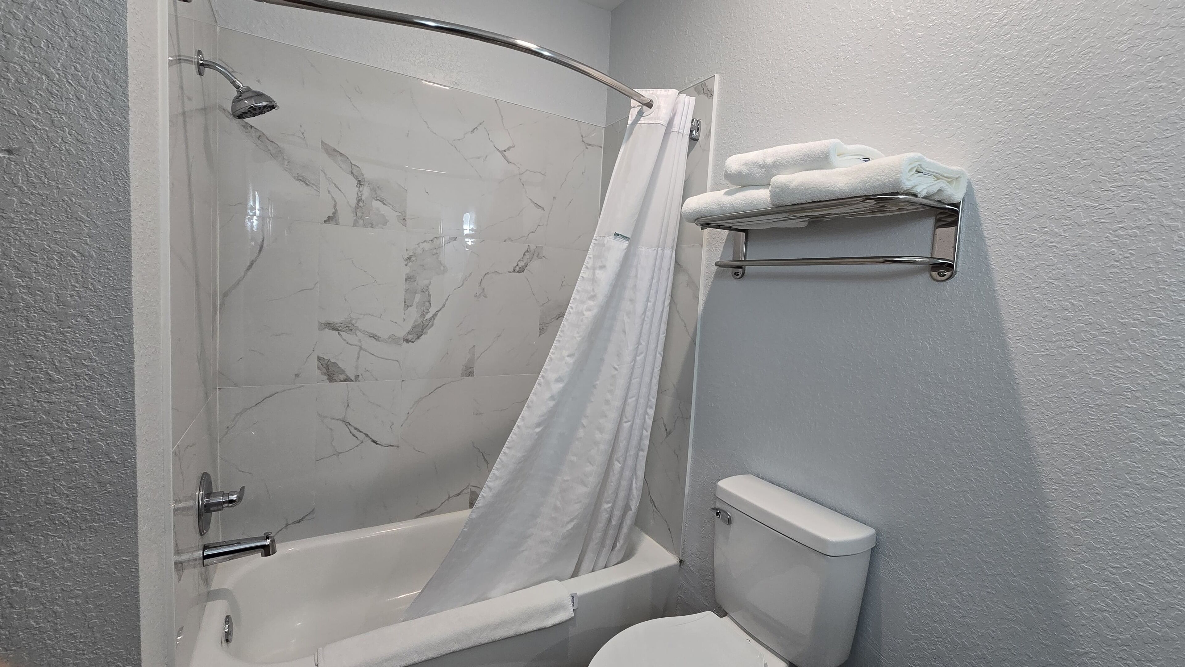 A bathroom with a shower, a toilet, and a towel rack with towels.