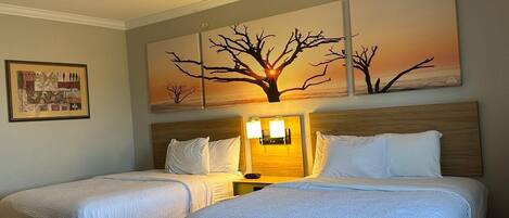 Habitación de hotel con dos camas, una mesita de noche con lámparas y un cuadro grande con un paisaje de árboles.