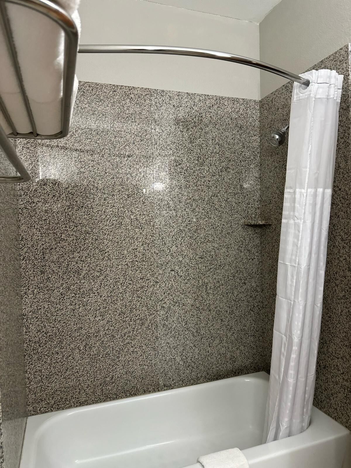 Ein Badezimmer mit Duschvorhang, Badewanne und Wandverkleidung aus Granitfliesen.