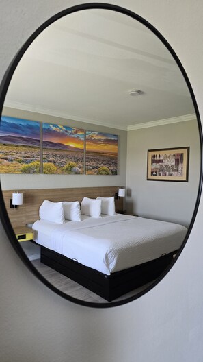 A bedroom with a bed, a nightstand, a wall-mounted lamp, a painting of a sunset, and a framed artwork. - Days Inn by Wyndham Copperas Cove (Copperas Cove)