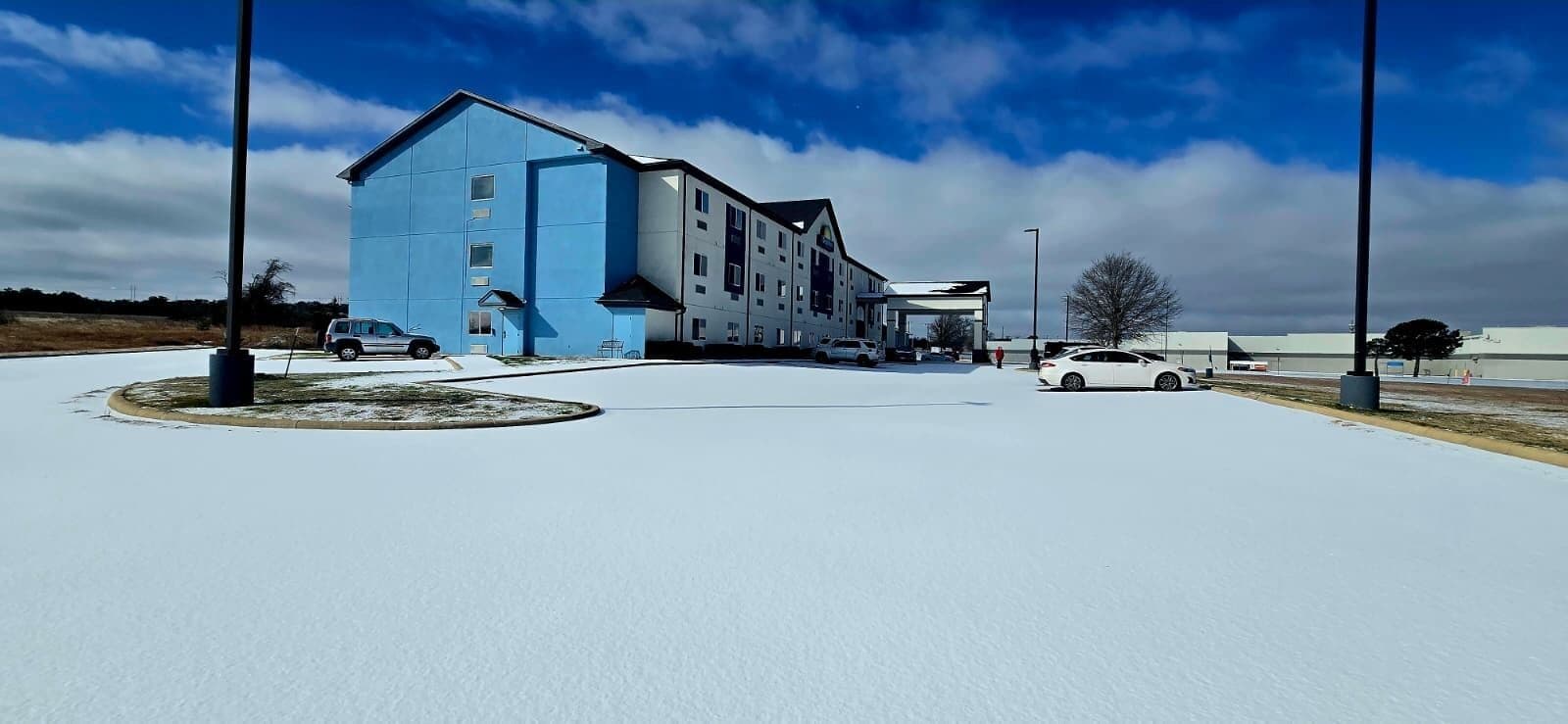 A hotel with a blue exterior, a covered parking area, and a clear sky.