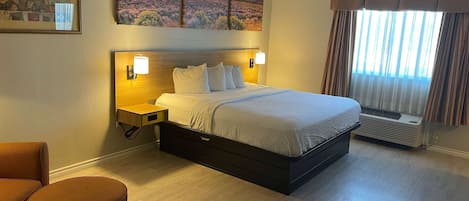 A hotel room with a large bed, bedside lamps, a nightstand, a chair, and a window with curtains.