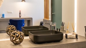 A modern kitchen with a curved island, pendant lighting, and a view of the living area. - George & Joanna Suites (Santorini)