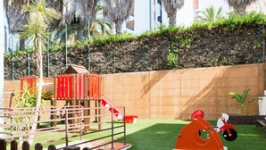 A playground with a slide and climbing structures, surrounded by a wooden fence and greenery. - APCOSTAS Las Mariposas / One Bedroom (Lloret de mar)