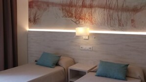 A hotel room with two beds, each with a teal pillow, a small bedside table, and a wall-mounted light. - APCOSTAS Las Mariposas / One Bedroom (Lloret de mar)