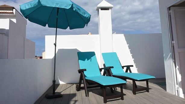 Eine Dachterrasse mit zwei Liegestühlen und einem blauen Sonnenschirm.