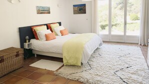 Una habitació amb un llit, una taula de nit, una làmpada, una cistella i vista a l'exterior a través d'una porta corredissa.
