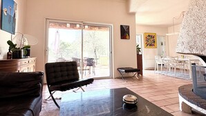 Zona d'estar àmplia amb un sofà negre, una taula de centre i zona de menjador amb cadires i taula.