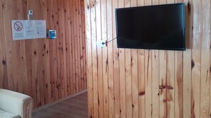 A room with wooden panel walls, a mounted flat-screen TV, a white air conditioning unit, and a sofa.