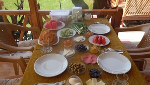 A dining table set with various food items and utensils, surrounded by chairs with floral cushions.