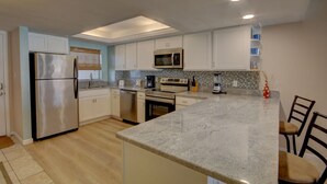 A modern kitchen with stainless steel appliances, white cabinetry, and a granite countertop.
