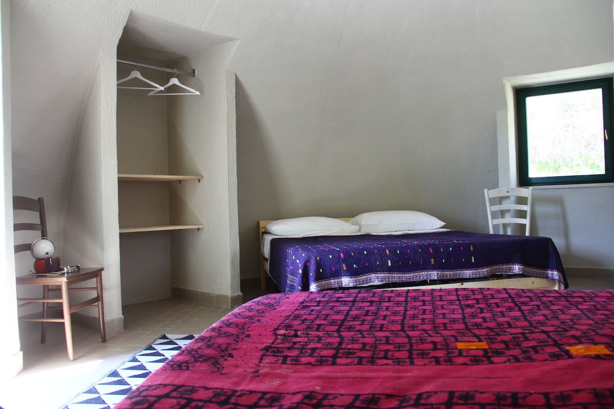Quarto com cama, cadeira, prateleira e janela.