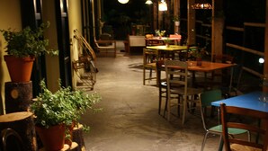 A narrow corridor with tables and chairs, potted plants, and hanging lights. - Astrocamp (Verghereto)