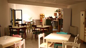 A dining area with multiple tables and chairs, a refrigerator, and shelves with various items. - Astrocamp (Verghereto)