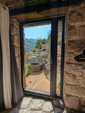 A stone-walled room with a wooden deck and a view of a mountainous landscape. - Renovated stone house in the heart of nature (Burzet)