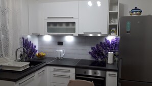 Una cocina moderna con armarios blancos, un refrigerador de acero inoxidable, un microondas y una tetera.