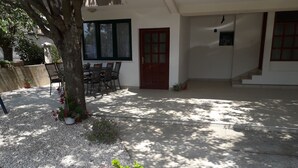 Un patio techado con una mesa, sillas, una planta en maceta y una puerta que da al interior.