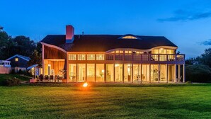 Une maison moderne dotée d’une grande façade vitrée, d’une vaste terrasse et d’un foyer extérieur dans le jardin.