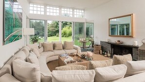 Un salon moderne doté d’un canapé aux lignes courbes, d’une cheminée et de grandes fenêtres donnant sur un paysage verdoyant.