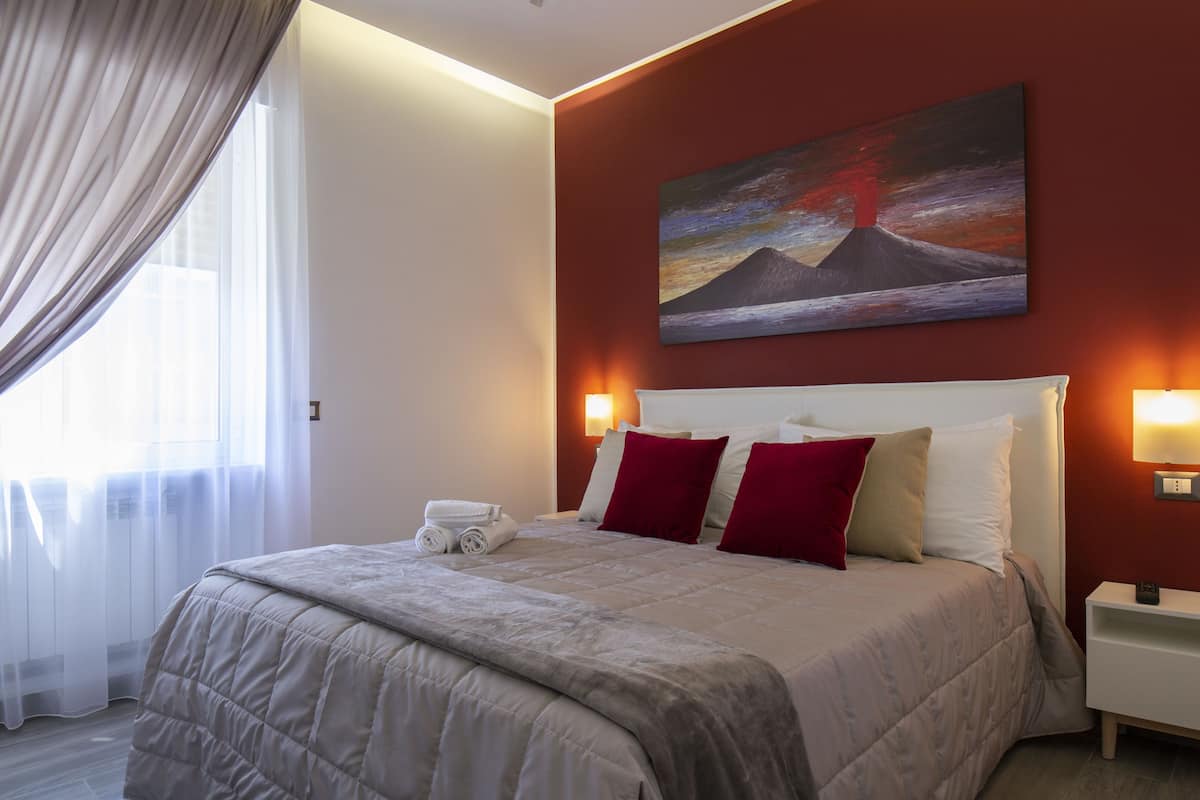 A hotel room with a large bed, a painting of a volcano, and a nightstand with a lamp.