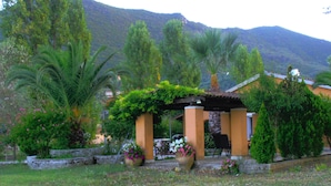 A garden with a pergola, palm trees, and a mountain backdrop. - Corfu Golf Countryhouse (Corfu)