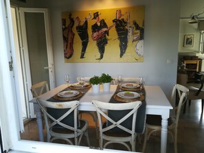 Un coin repas avec une table blanche dressée pour quatre personnes, entourée de chaises blanches. Un grand tableau abstrait est accroché au mur au-dessus de la table.