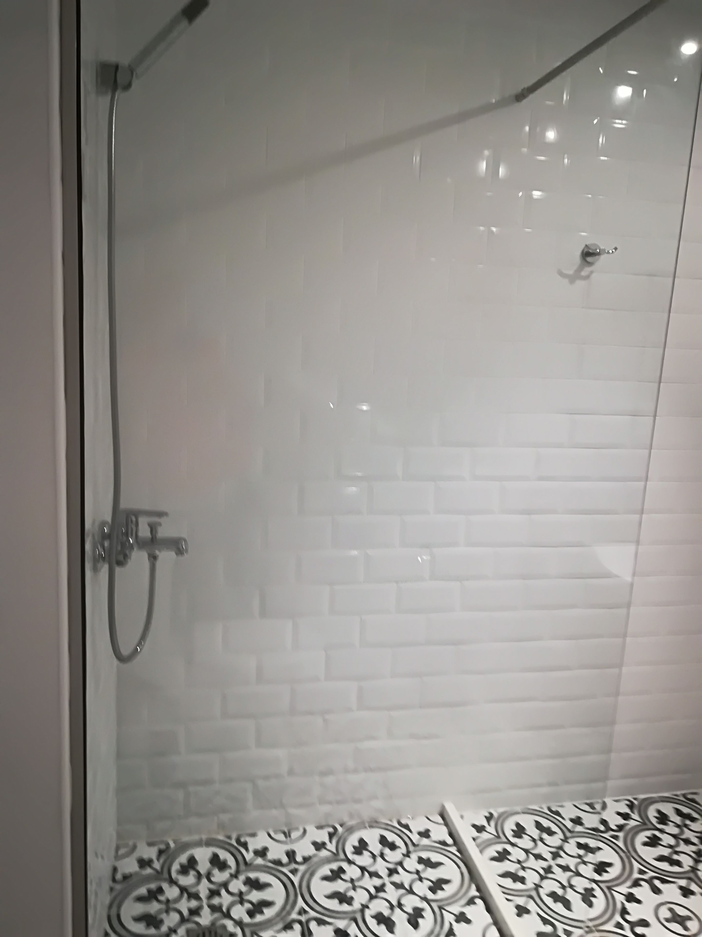 En dusch med glasväggar, vita kakelplattor på väggarna och ett mönstrat golv.
