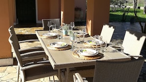 An outdoor dining area with a table set for four, surrounded by wicker chairs, and a view of a garden and mountains in the background. - Corfu Golf Countryhouse (Corfu)