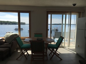A dining area with a table and chairs, large windows with a view of a lake and boats, and a sliding glass door leading to an outdoor balcony.