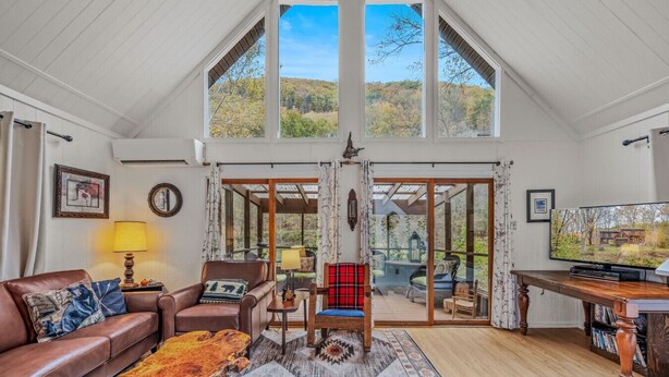 A spacious living room with a high ceiling, a large window, and a cozy seating area. - River Time Cabin -riverfront, wifi, screen porch, 3 king beds, view, wood stove (Great Cacapon)