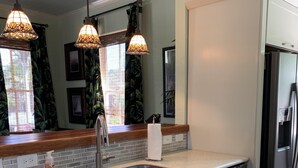 A kitchen with white cabinets, a stainless steel sink, and a built-in dishwasher. There are three pendant lights hanging above the sink. - Stylish 2 BED, 2 BATH Shotgun-style house near beach! (Galveston)