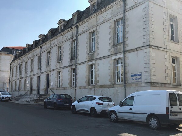 A historic building with multiple windows and a sign indicating it is a residence. Several cars are parked in front.