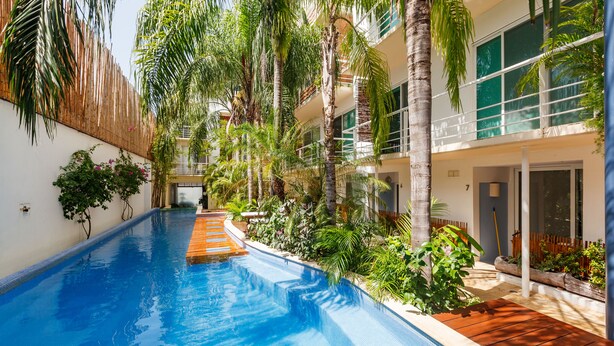 A swimming pool surrounded by lush greenery and a modern building with large windows. - La Papaya- Luxury Condo-complete apartment in PDC (Playa del Carmen)