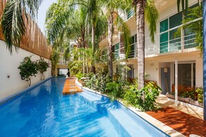Una piscina rodeada de abundante vegetación y un edificio moderno con grandes ventanales.