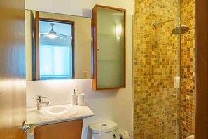 A bathroom with a white sink, a toilet, a mirror, and a shower with mosaic tiles.