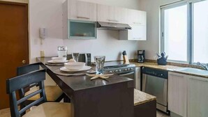 A compact kitchen with a central island, a stove, dishwasher, and a window providing natural light. - La Papaya- Luxury Condo-complete apartment in PDC (Playa del Carmen)
