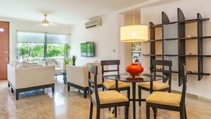 A modern living room with a glass dining table, black chairs, a red lamp, and a TV mounted on the wall. - La Papaya- Luxury Condo-complete apartment in PDC (Playa del Carmen)