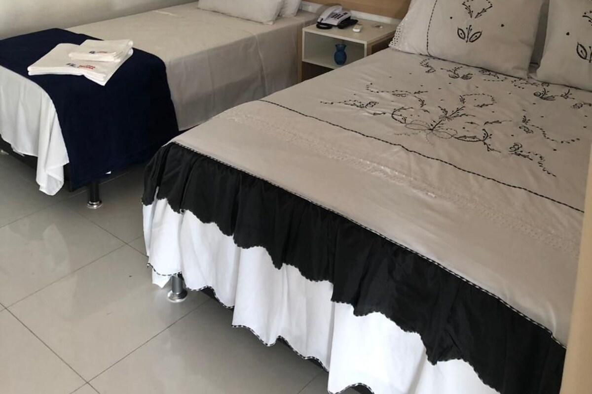 Habitación de hotel con dos camas, cortinas color crema, una mesita de noche con teléfono y un cuadro de una puesta de sol.