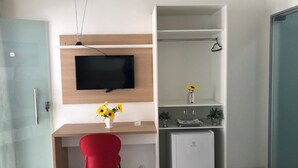 Una habitación moderna con un escritorio de madera, una silla roja, un televisor, un refrigerador pequeño y un armario empotrado.
