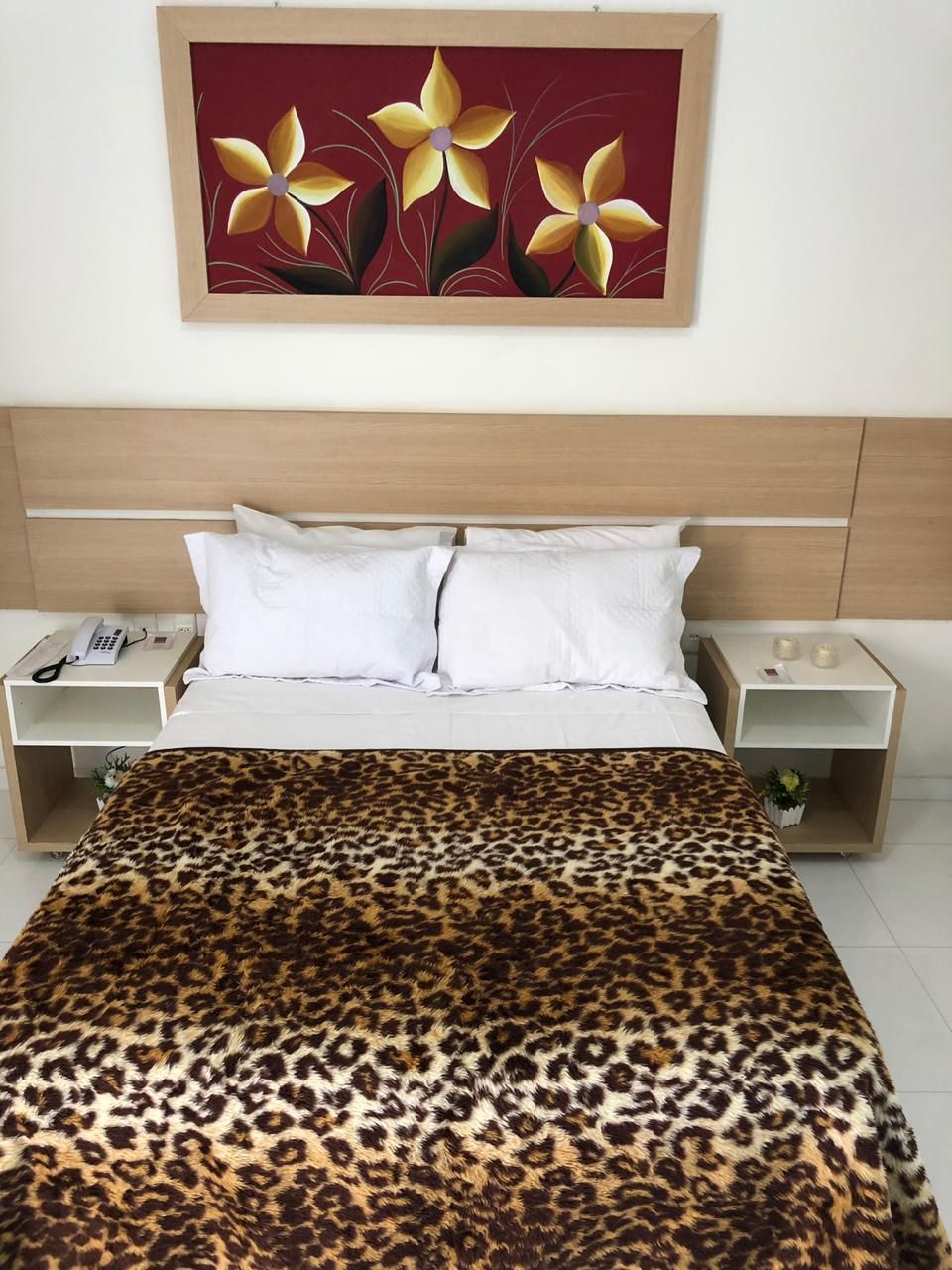 A hotel room with a bed, two bedside tables, a telephone, and a painting on the wall.