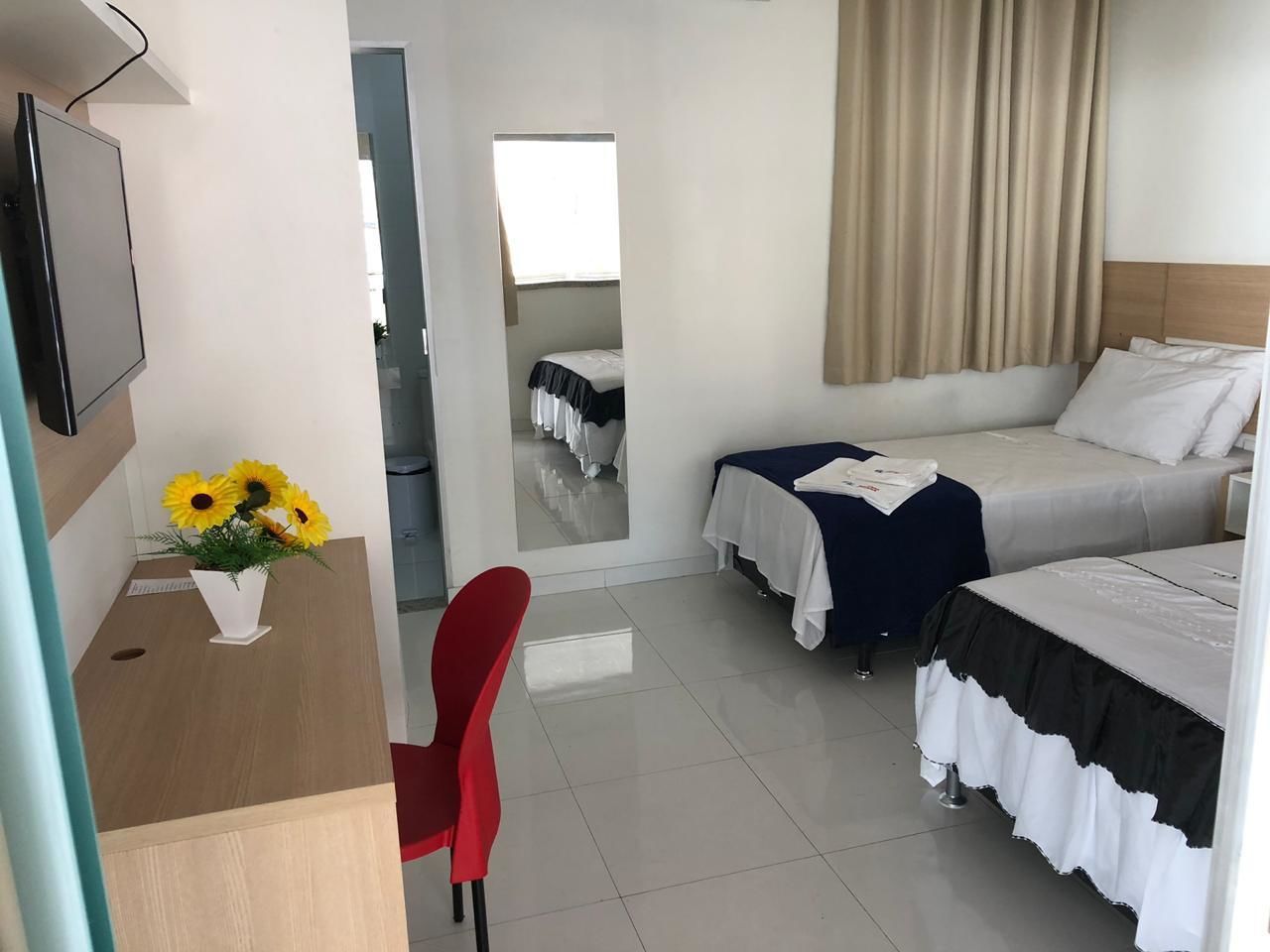 A hotel room with two beds, a desk with a chair, a TV, and a vase of sunflowers.