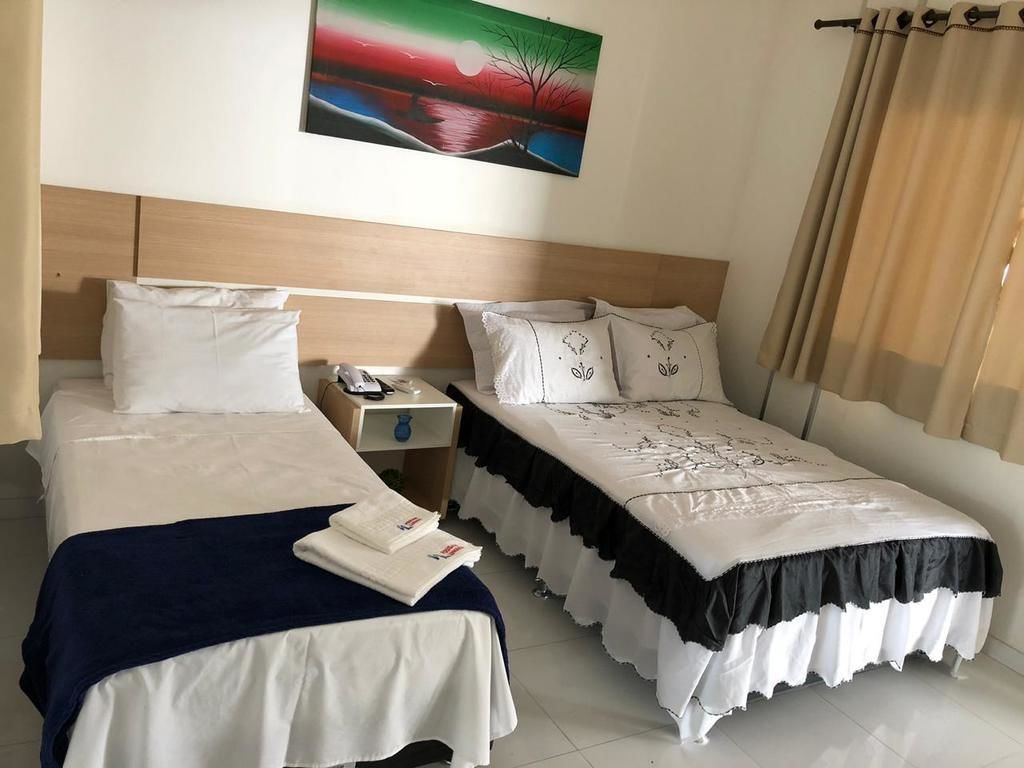 A hotel room with two beds, a nightstand, a phone, and a painting on the wall.